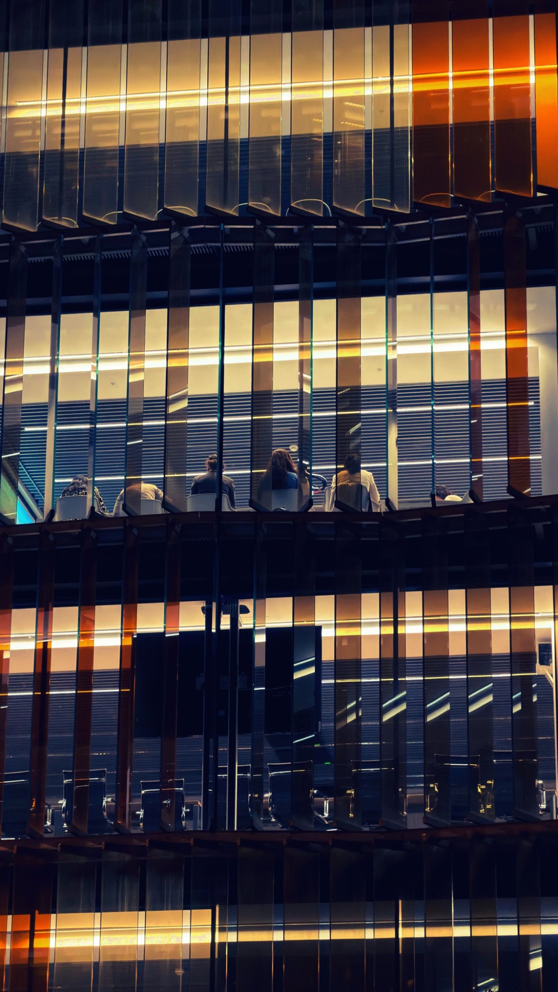A team meeting in a lit office at night, seen through a glass facade